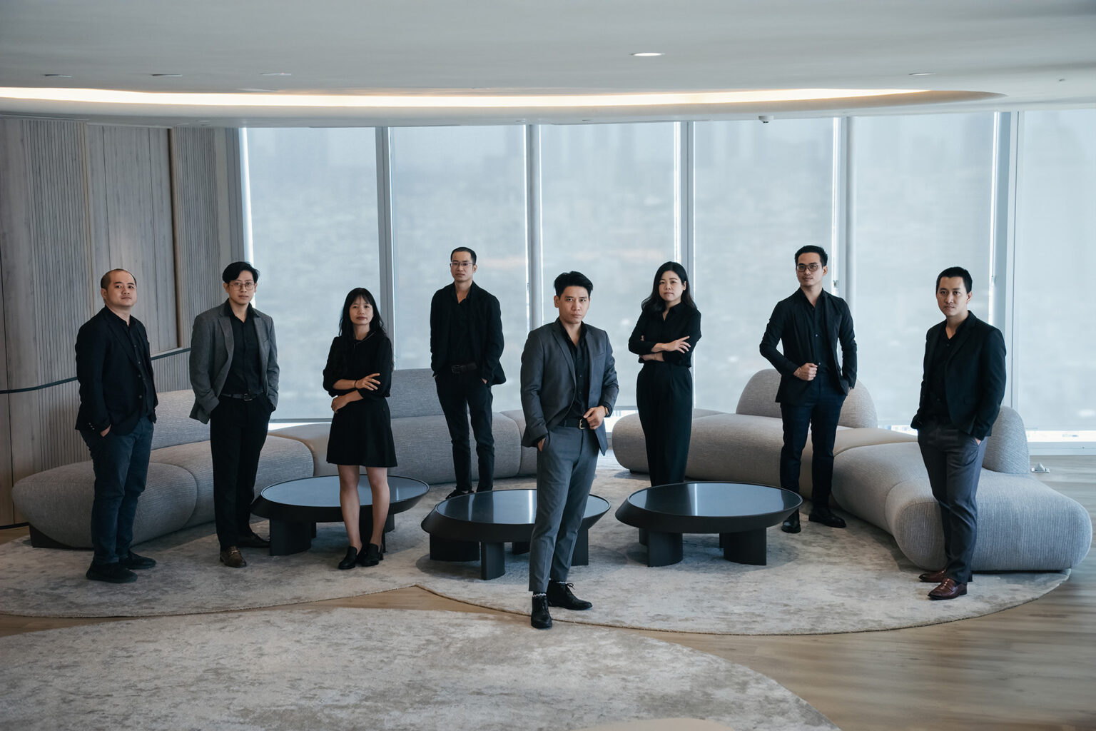 Chụp ảnh profile công ty doanh nghiệp: ban lãnh đạo khoảng 9 người mặc trang phục tối màu đứng dàn hàng trước cửa kính lớn