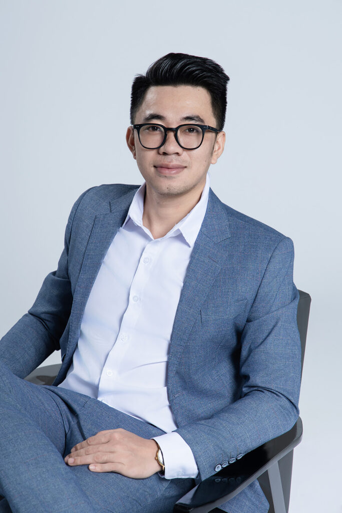 Biến thể ảnh profile LinkedIn: nam mặc vest xám xanh, sơ mi trắng mở cổ không cà vạt, ngồi ghế vắt chân, cười nhẹ