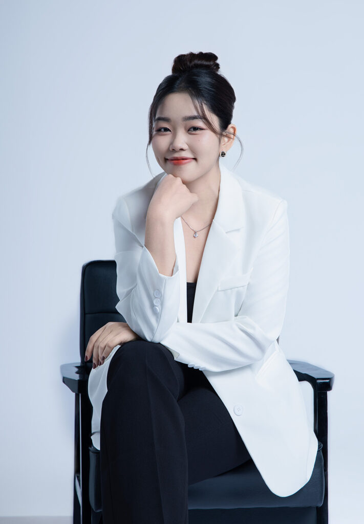 Ảnh profile cá nhân năng động: nữ trẻ búi tóc, blazer trắng, ngồi ghế đen chống cằm cười tươi trên nền trơn sáng