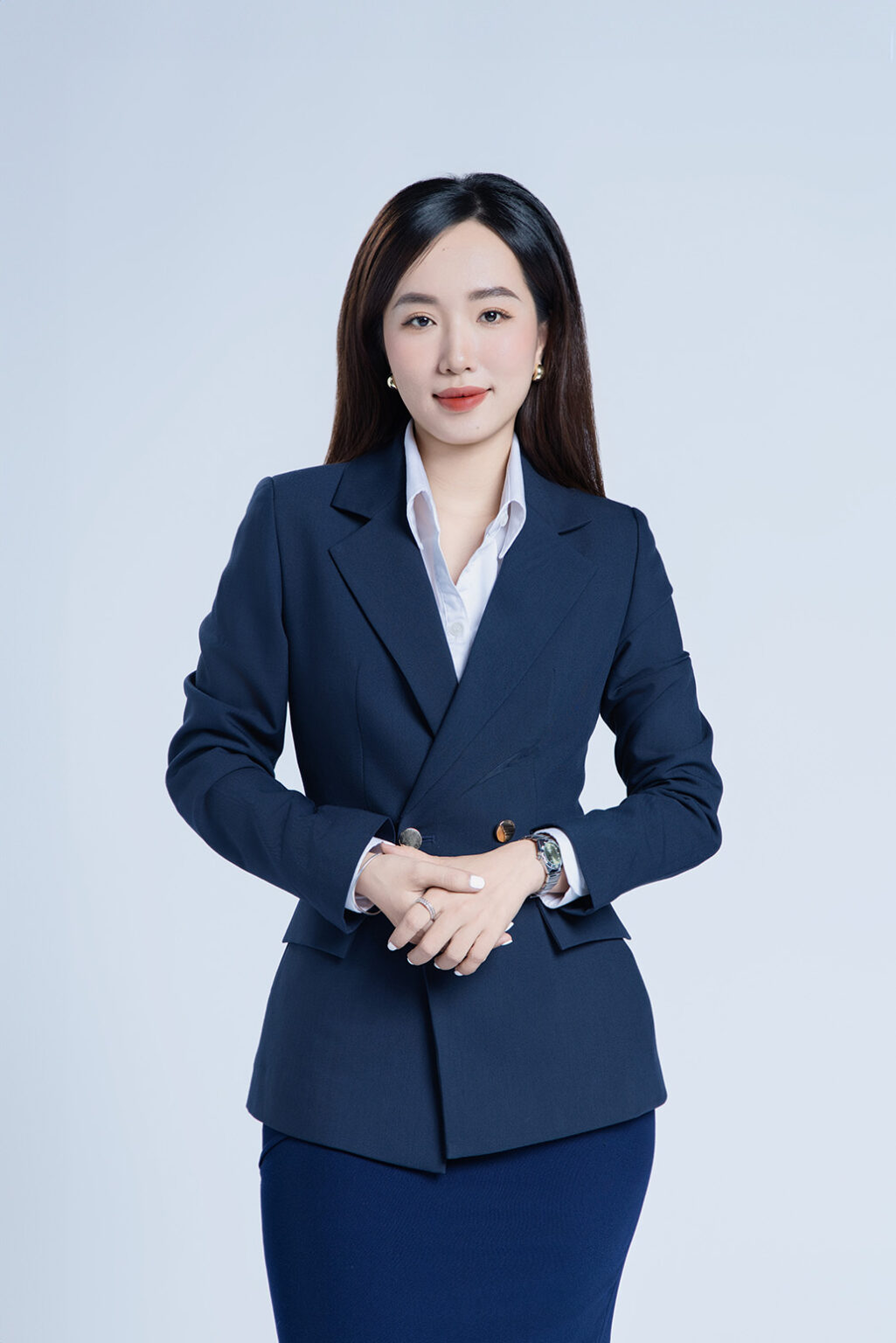 Chụp ảnh profile LinkedIn chuyên nghiệp: nữ mặc blazer navy, sơ mi trắng, hai tay đan trước bụng, cười mỉm trên nền trơn