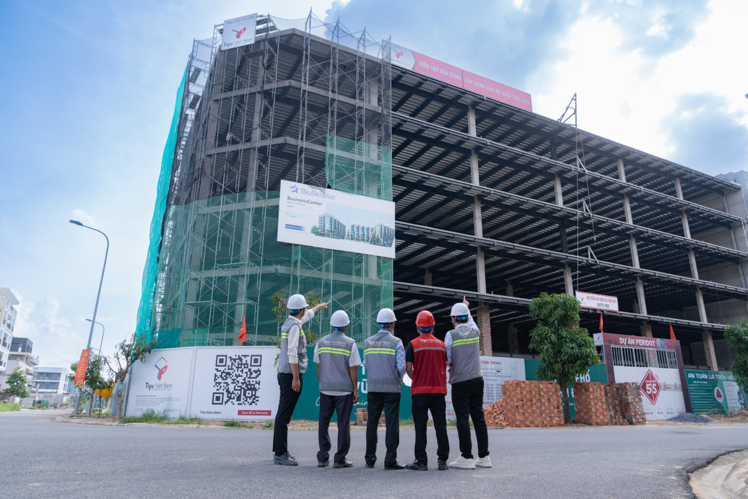Ảnh profile công ty xây dựng: năm người mặc áo phản quang, đội mũ bảo hộ đứng quay lưng, một người chỉ tay lên tòa nhà đang thi công