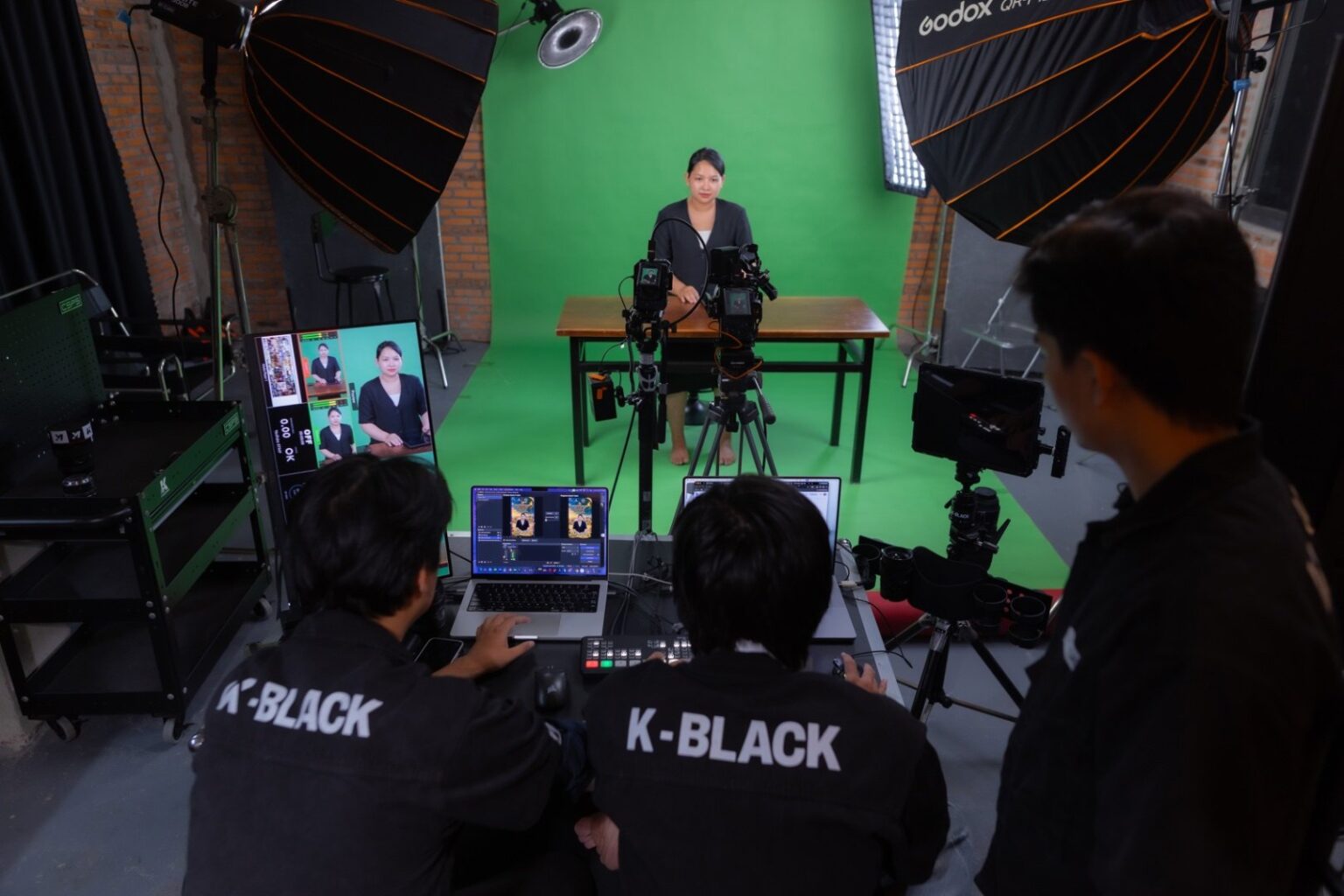 Kỹ thuật viên K-BLACK vận hành laptop và bàn switcher trong buổi livestream sự kiện online, nữ host ngồi bàn phía trước